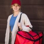 Young woman delivery worker holding a red insulated bag, ready to deliver food. Casual and friendly vibe.